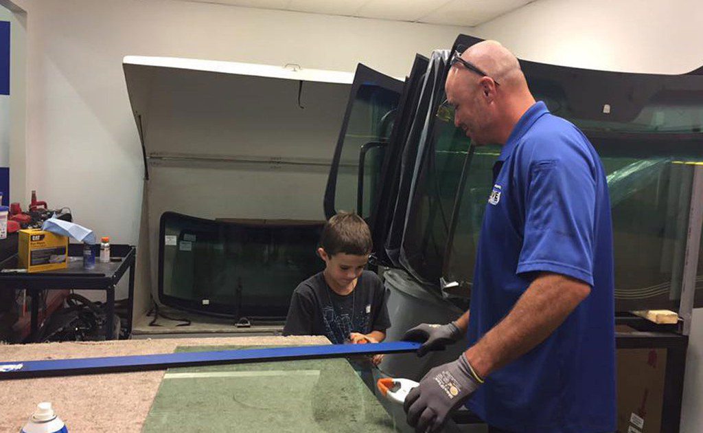 Man and boy installing car windshield.